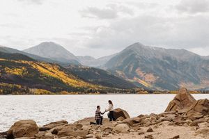 Couple sharing a marriage proposal on rocky lakeside with stunning mountain backdrop and autumn foliage in Colorado.