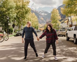 Couple holding hands walking on a street in Telluride, Colorado, with fall foliage and mountain backdrop.