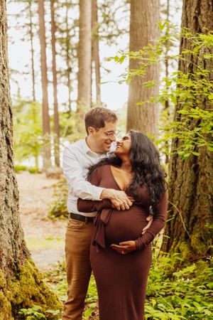 Romantic couple embracing and laughing together in a sunlit forest setting.