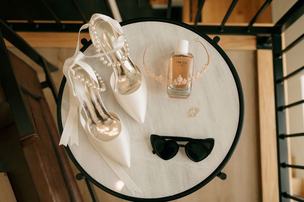 Wedding accessories including silver heels and sunglasses arranged on a round table.