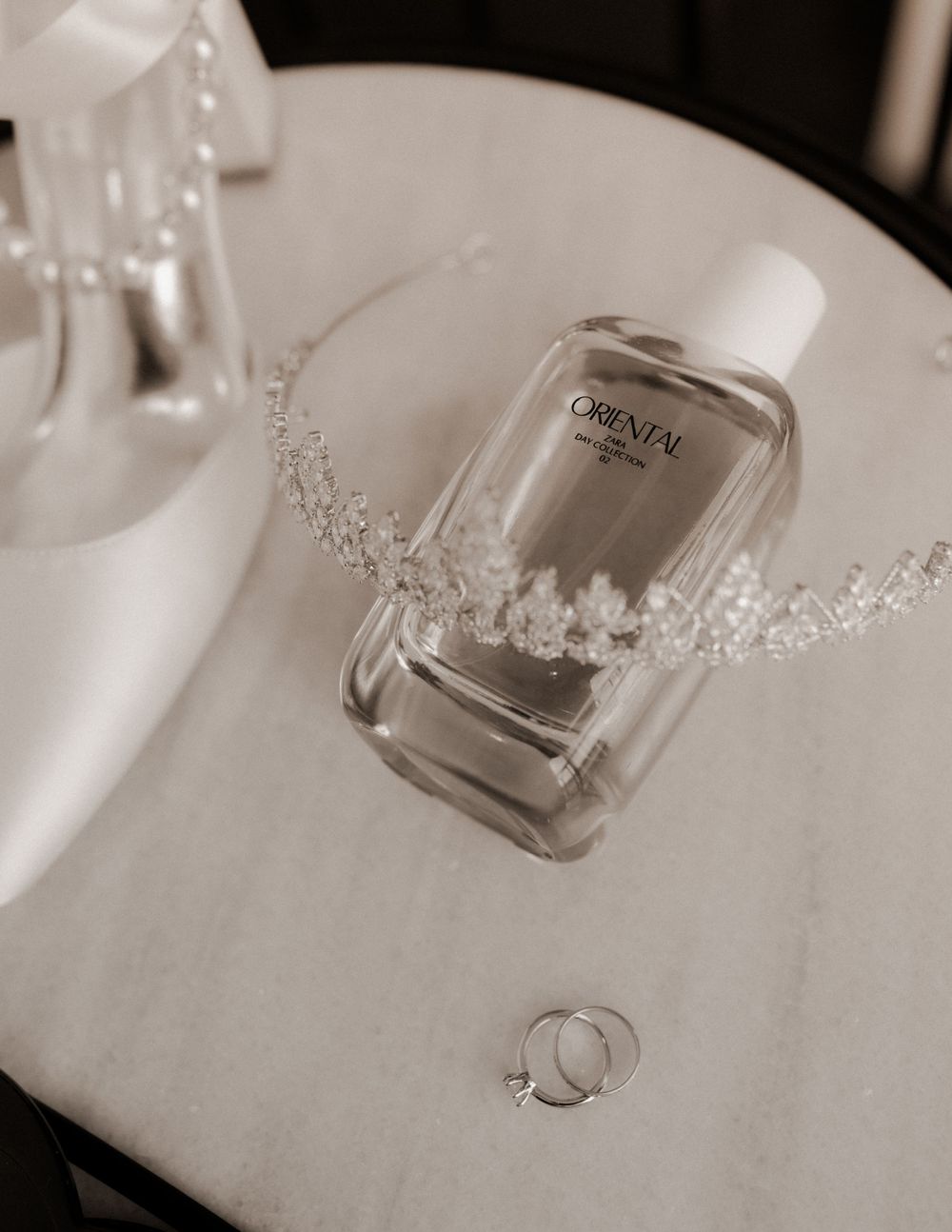 Wedding details featuring perfume bottle, delicate tiara and wedding rings on white surface.