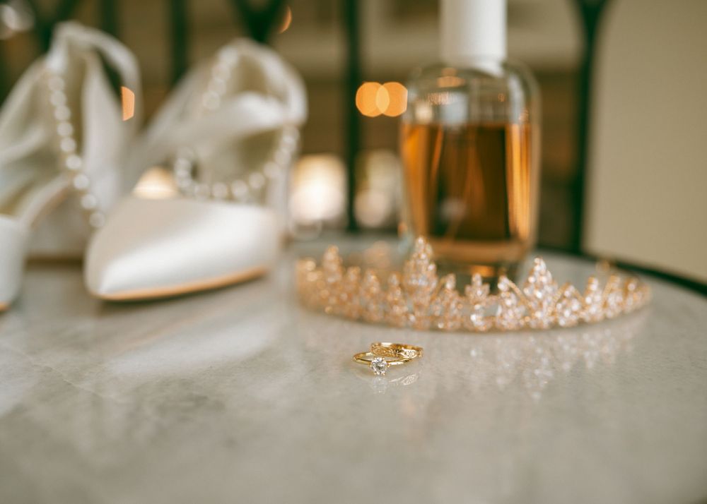 Wedding accessories including white shoes, a delicate crown, and rings arranged with champagne.
