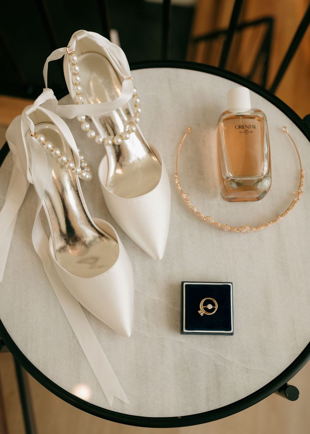 Wedding accessories including white heels, perfume bottle and jewelry box arranged on a round table.