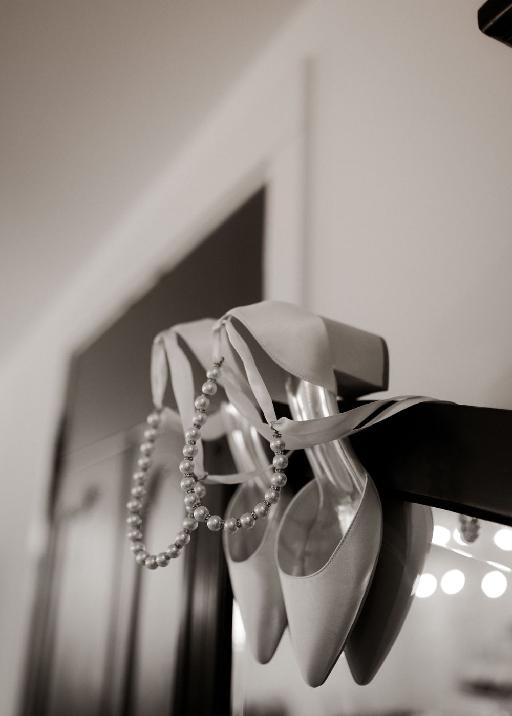 Wedding shoes and pearl necklace hanging together in black and white photography.
