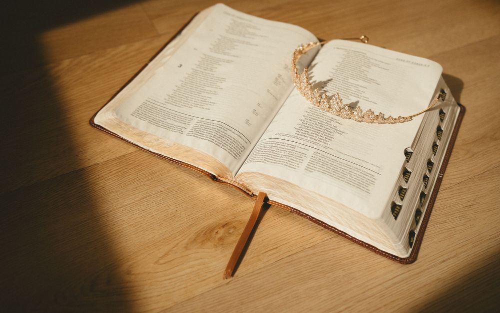An open Bible with a delicate rose gold crown placed on its pages in warm lighting.