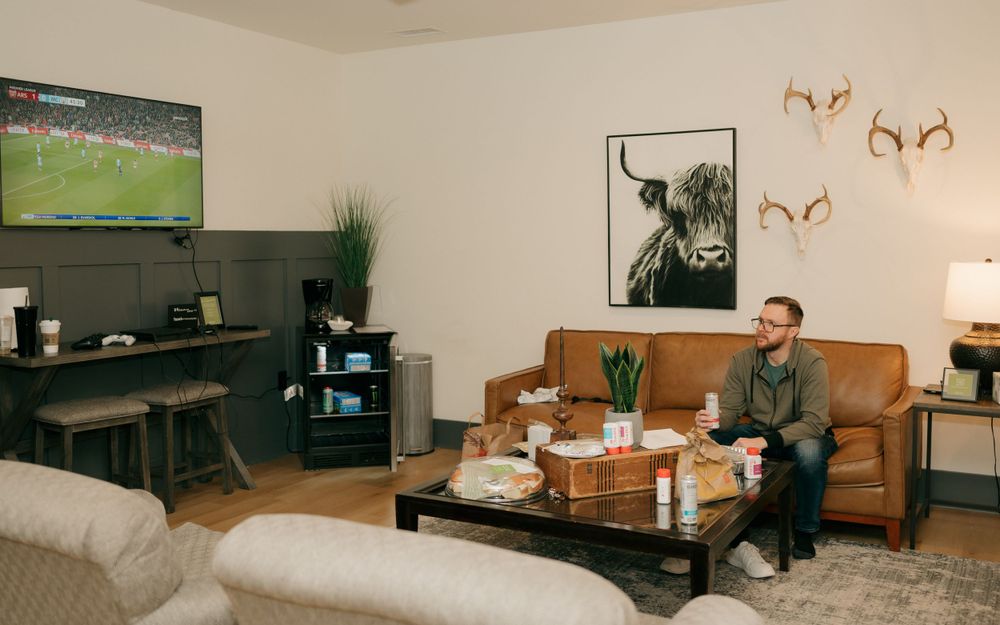 A modern living room with sports on TV, leather couch, and wall art decorations.