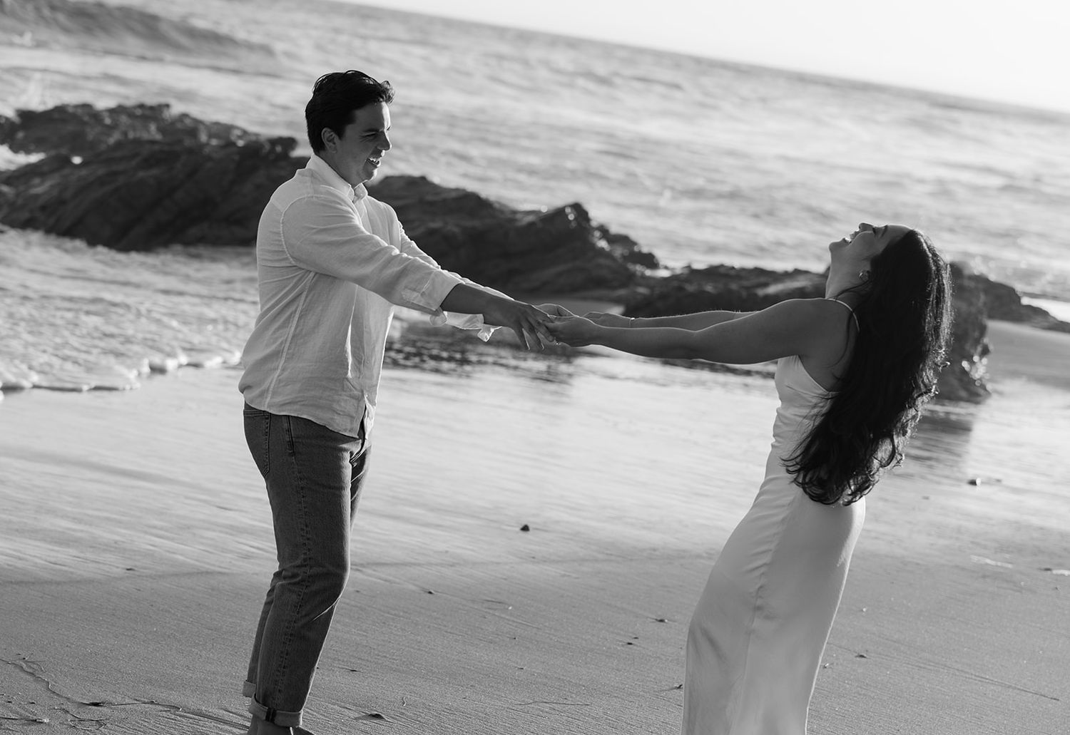 Black and white photo of couple in romantic embrace on beach with waves crashing.