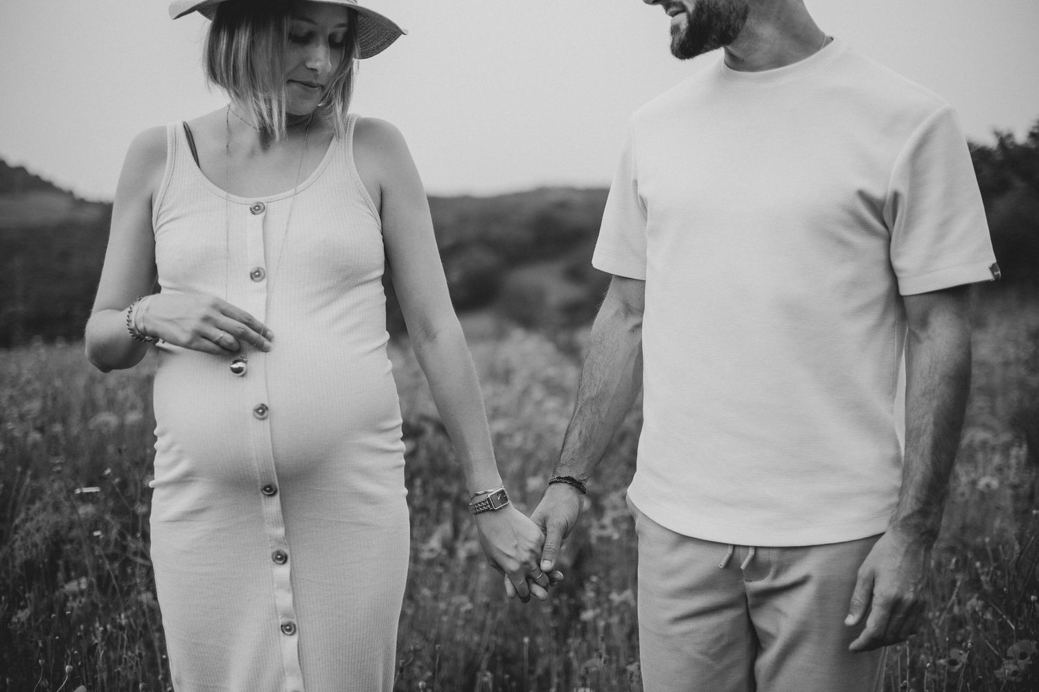 Photo en noir et blanc d'un couple lors d'une séance maternité. La femme enceinte tient la main de son partenaire.