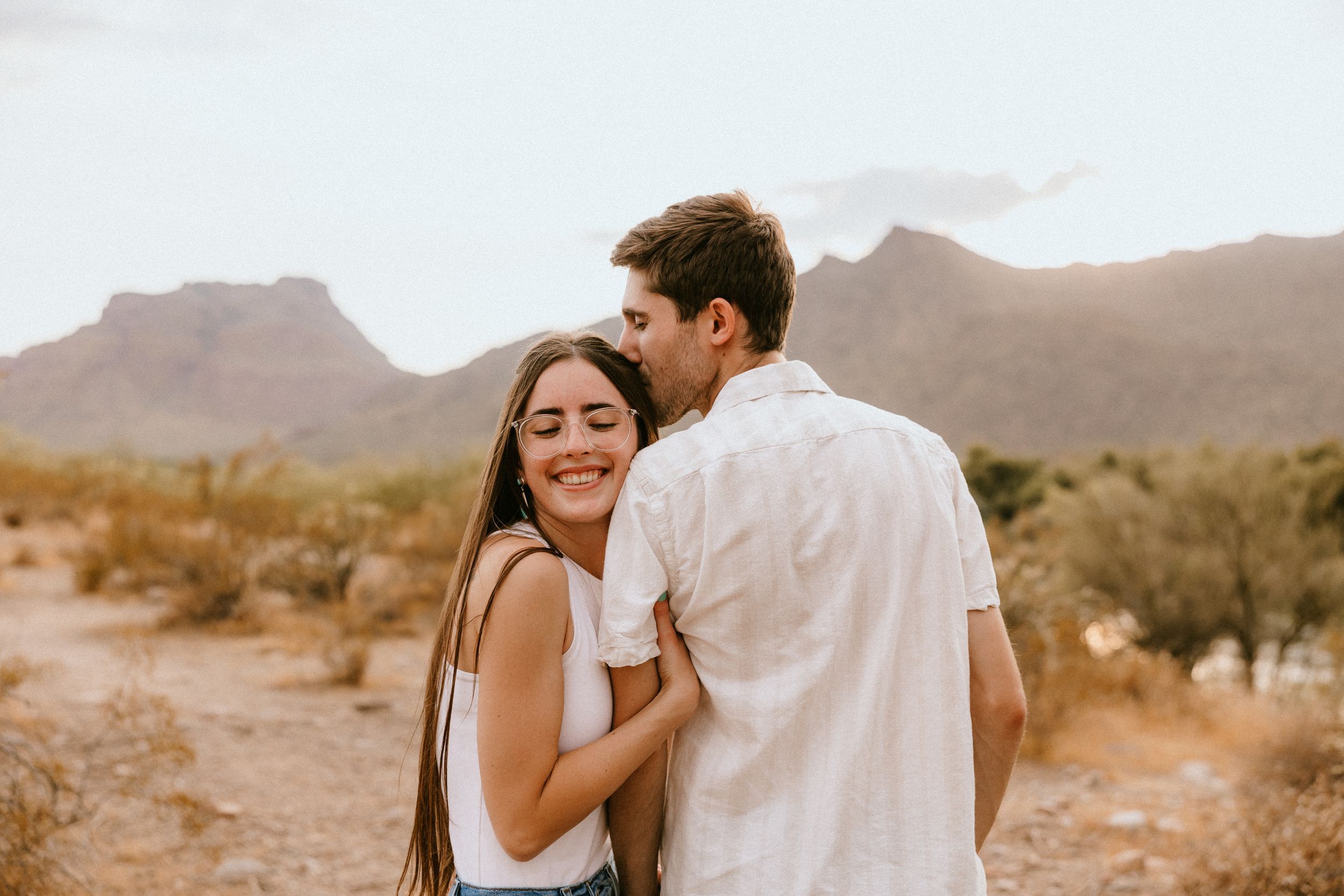 A romantic embrace between a couple on a desert trail during sunset.