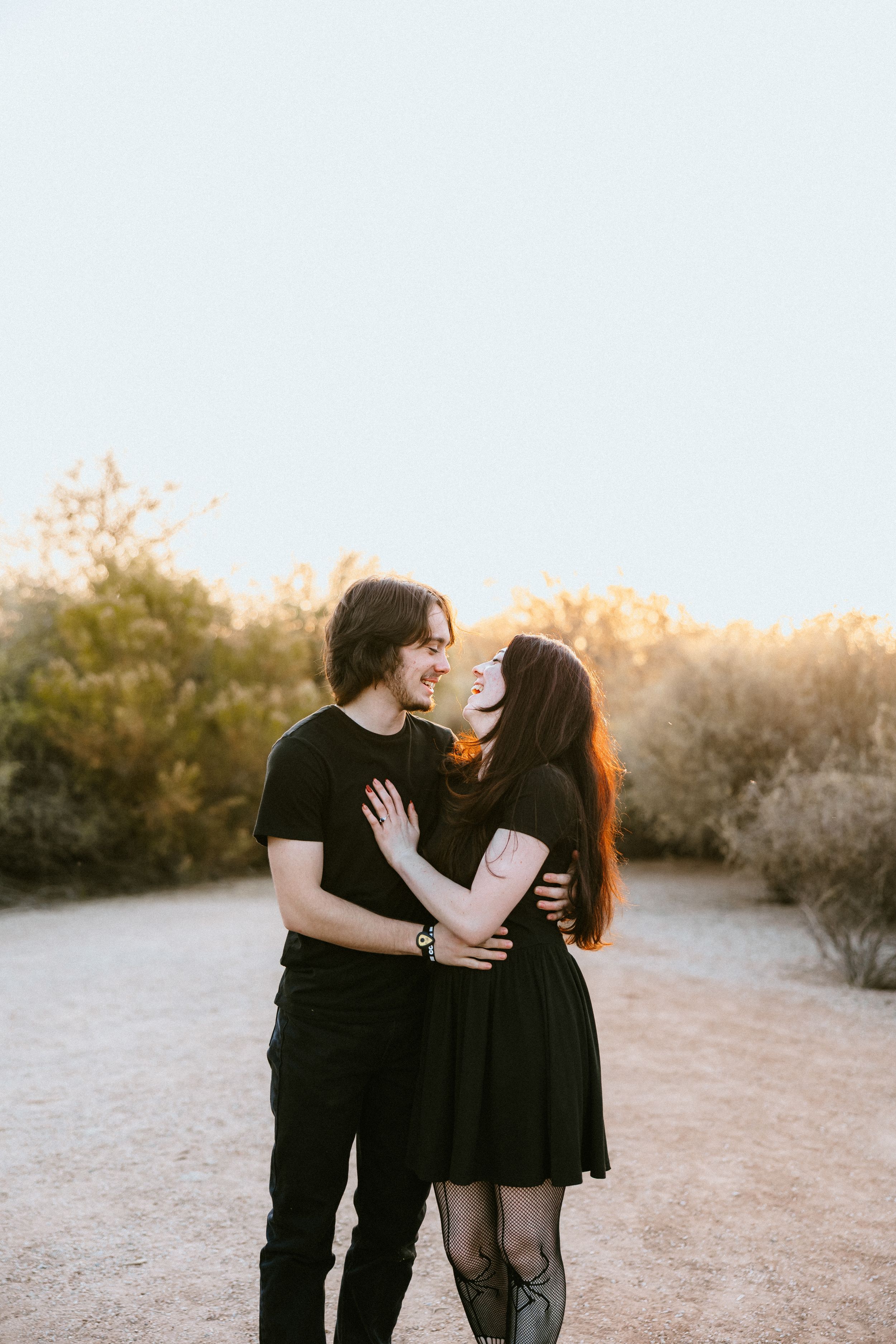 A couple in matching black outfits share a romantic moment on a desert path at golden hour.
