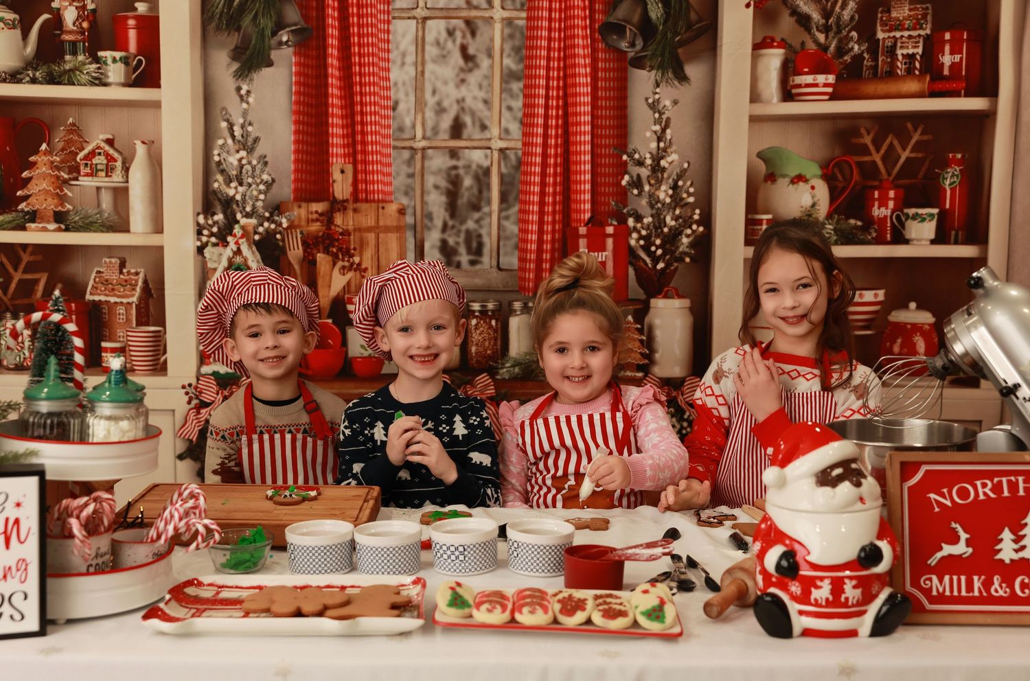 Four children baking Christmas cookies together in a festive holiday kitchen decorated with red and green ornaments.