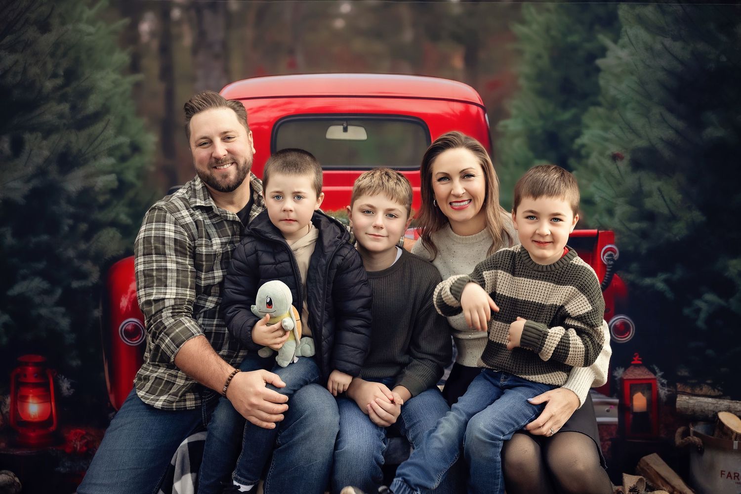 Family of five posing on red vintage truck tailgate surrounded by Christmas trees in festive holiday photo.