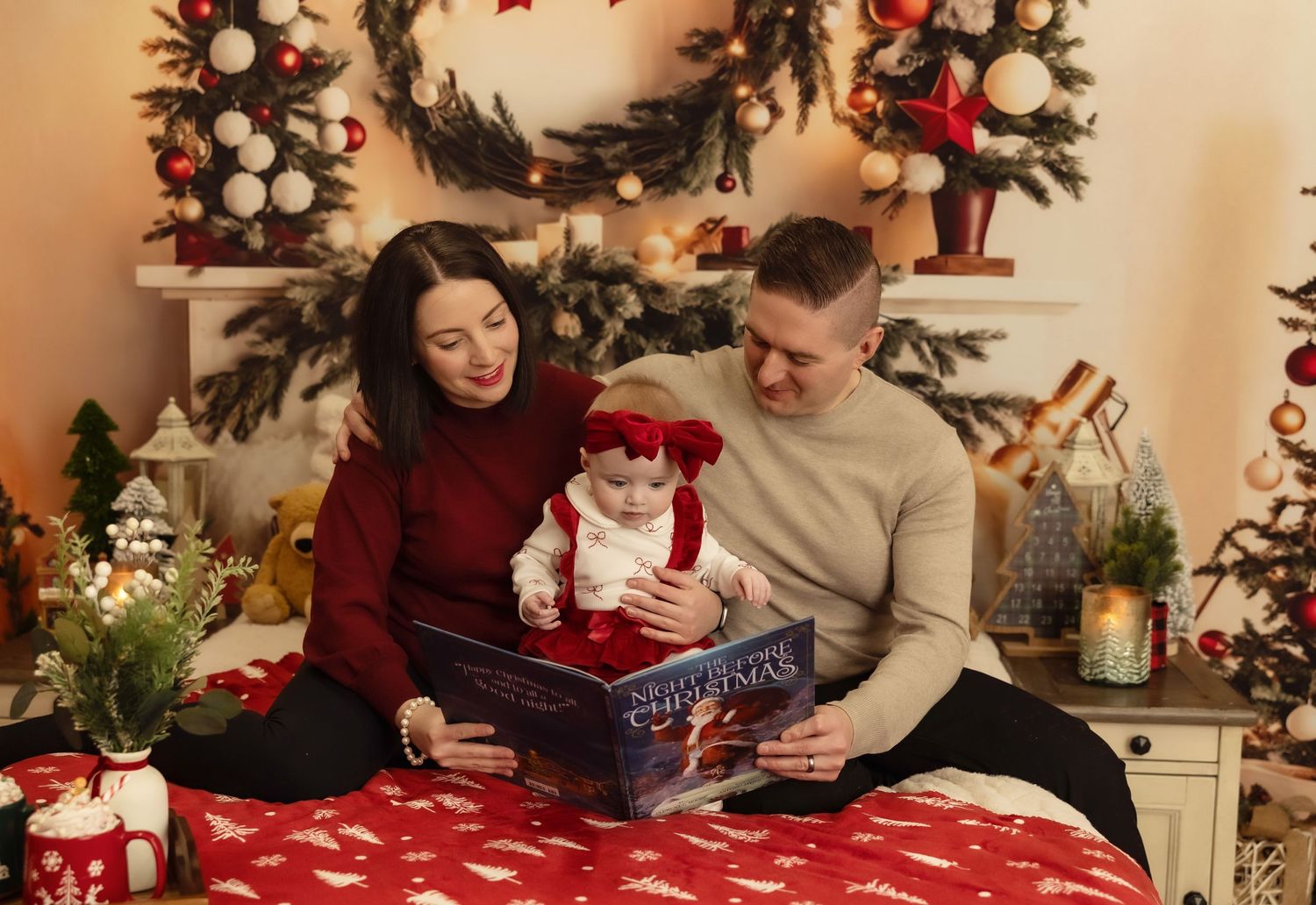 Family with baby reading a Christmas book on a festive decorated bed with holiday wreath and lights.