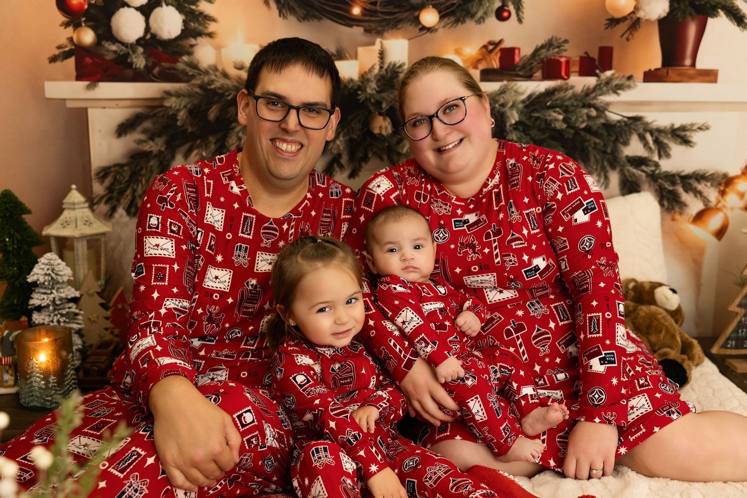 Family of four in matching red Christmas pajamas posing together in front of a decorated holiday tree.