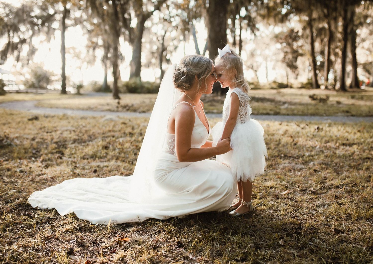 A tender moment between a bride and young child on a sunlit autumn day beneath Spanish moss-draped trees.