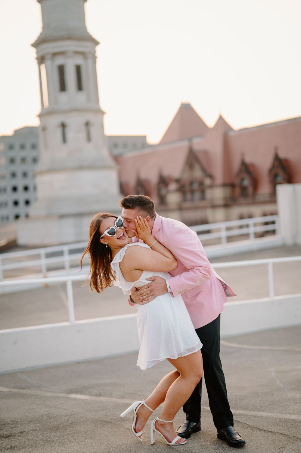Romantic dance pose on rooftop with church spire in background during sunset.
