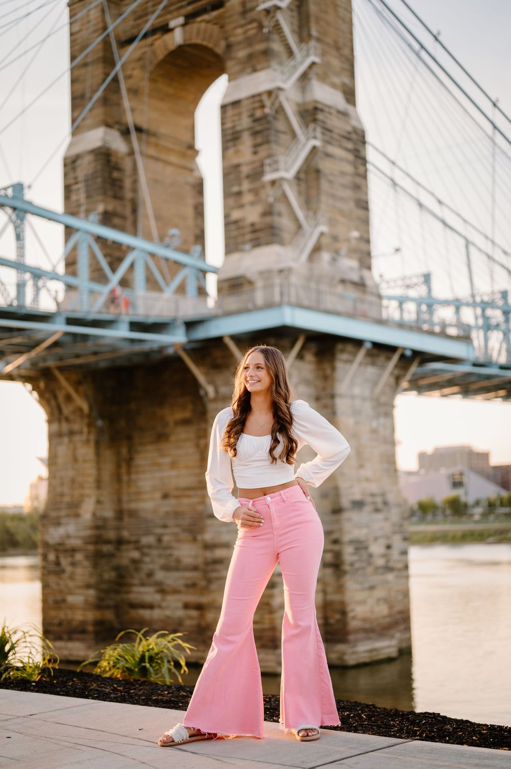Fashion portrait near historic bridge featuring pink bell bottom pants and white top.