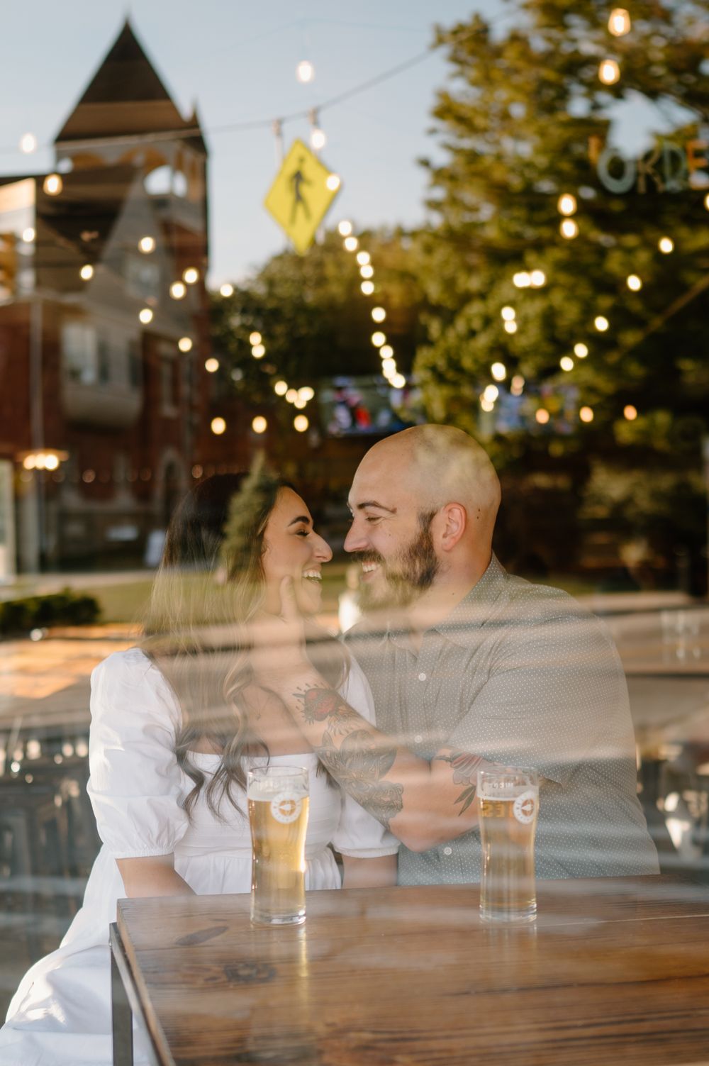 Romantic evening scene through window with string lights and beer glasses on table.