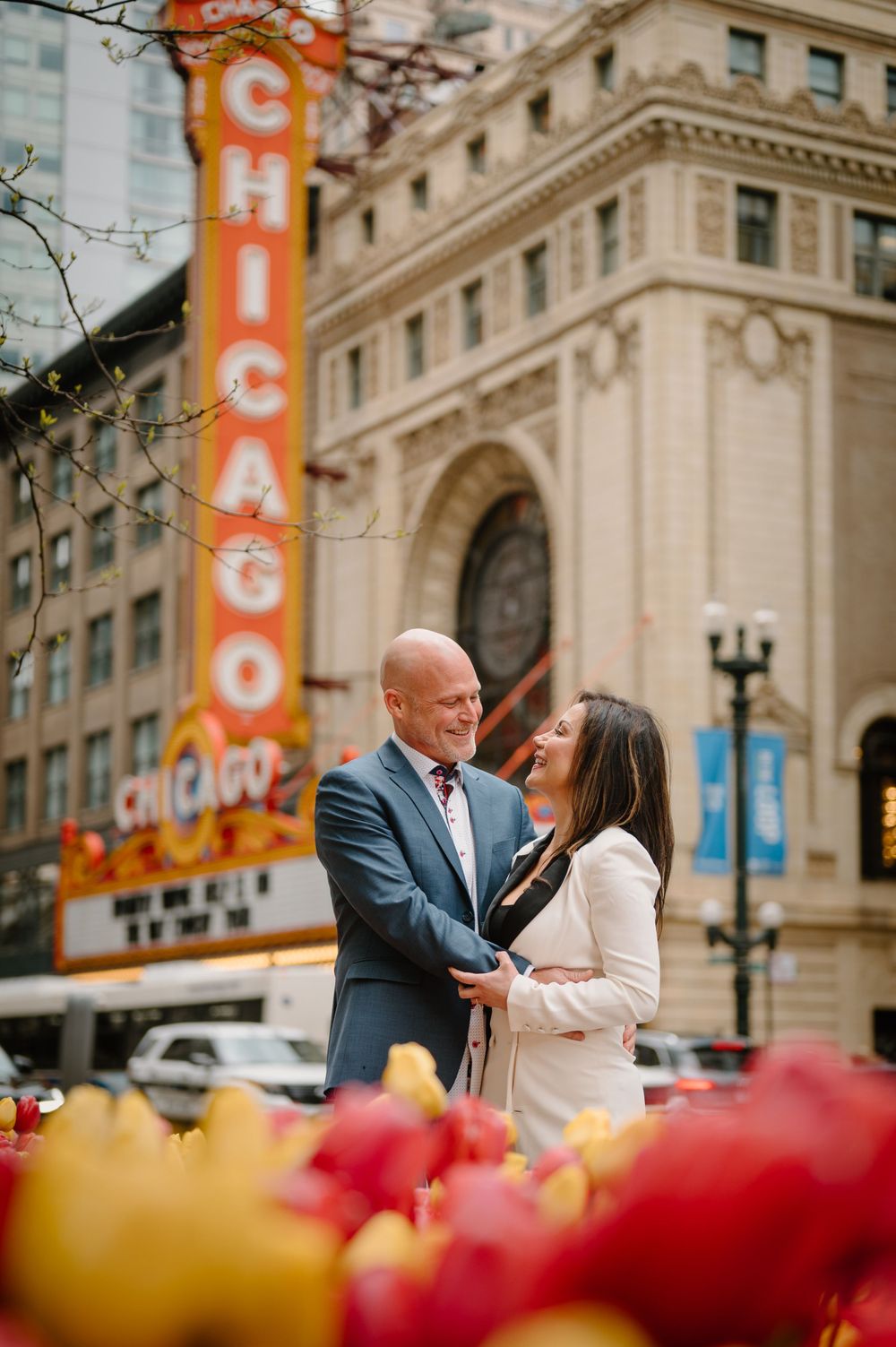 Couple embracing in front of iconic Chicago Theater sign with tulips in foreground.