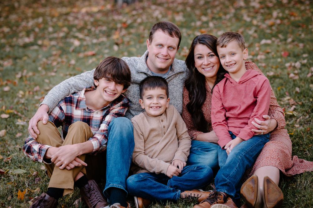 Casual fall family portrait on grass with autumn leaves in background.