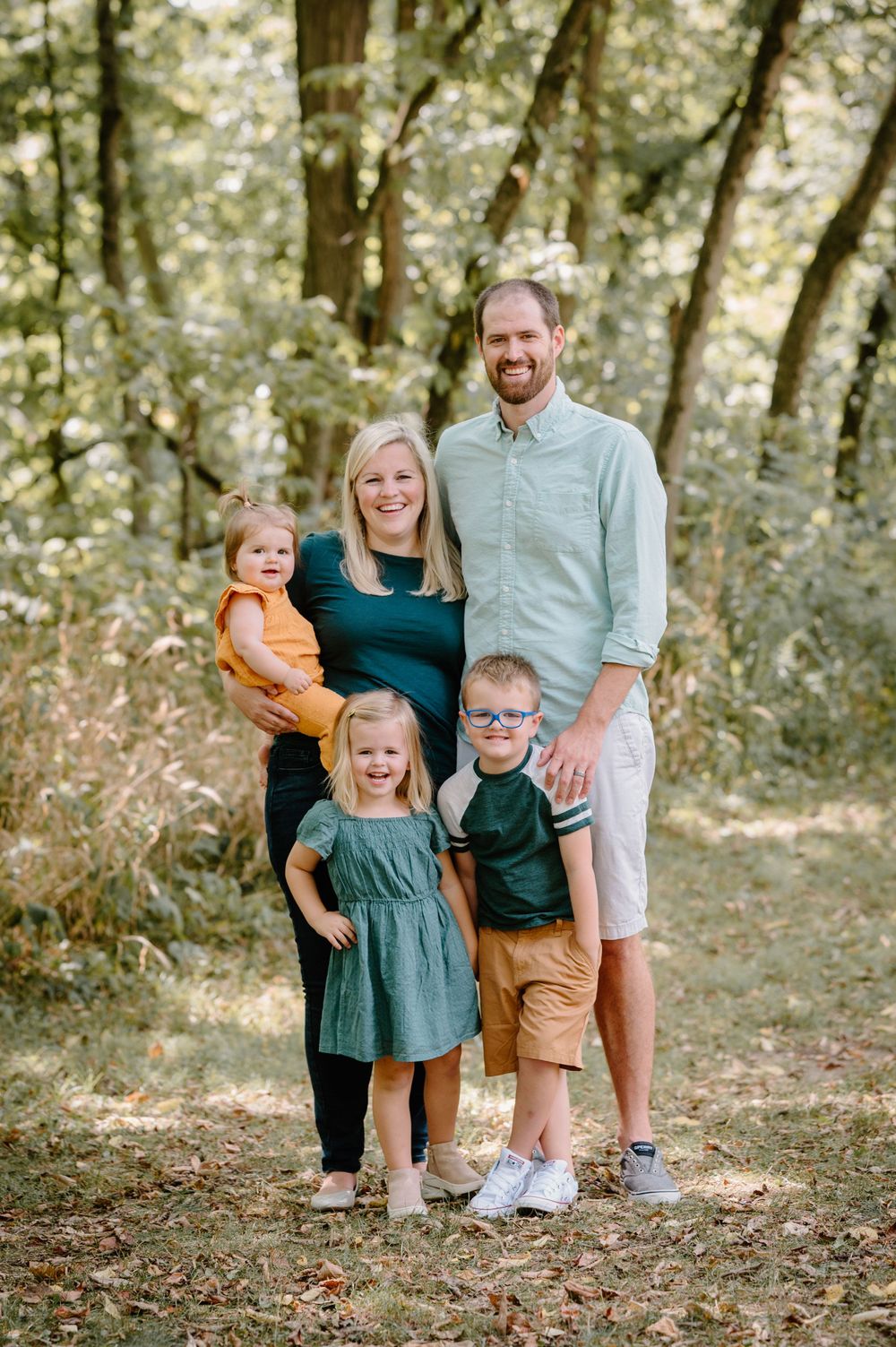 Happy family of five posing together in casual clothes against wooded background.