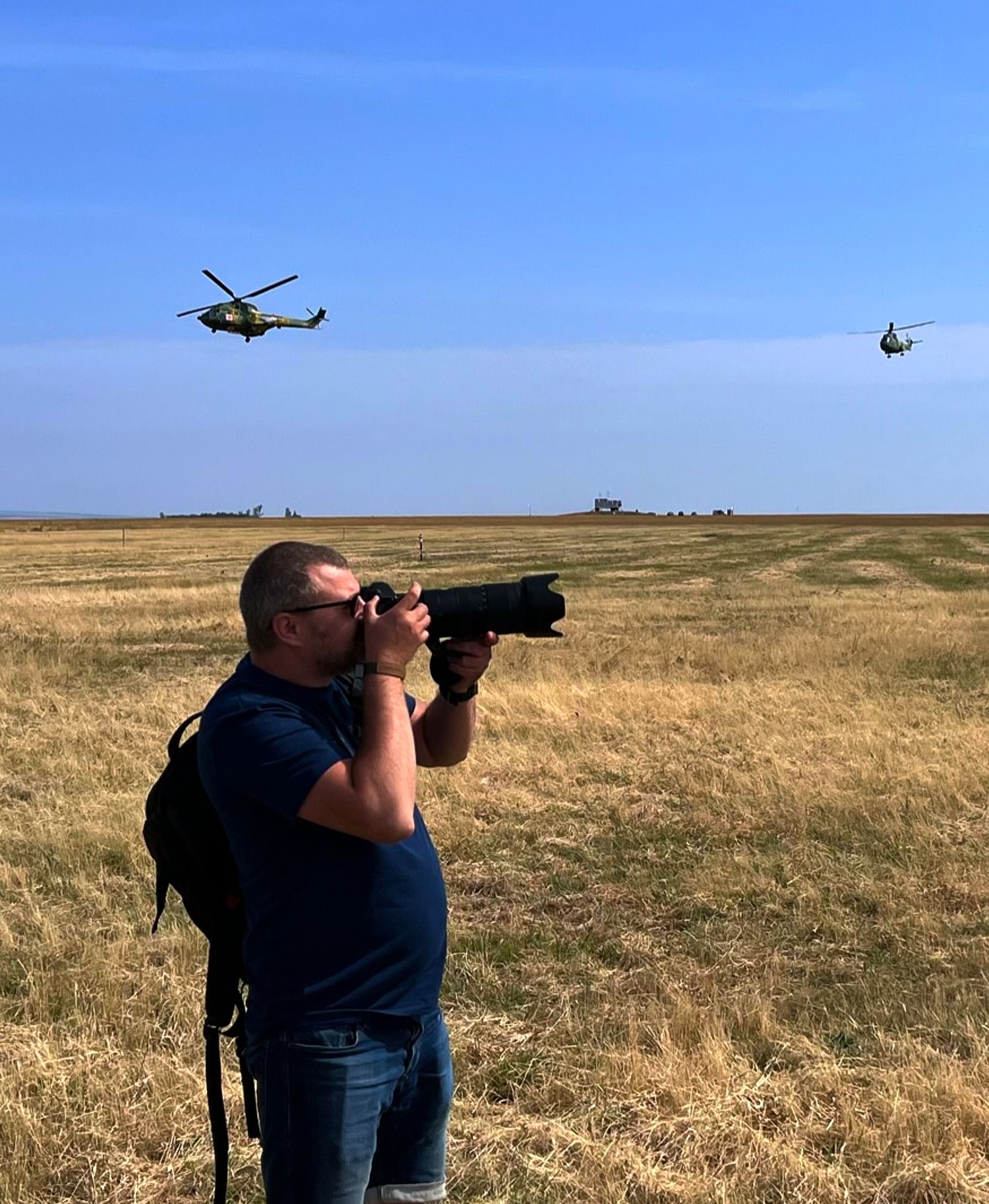 Photographer with telephoto lens captures helicopters flying over dry grassland.