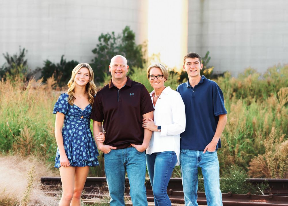 A family group wearing casual clothing poses together outdoors in a rustic setting during golden hour.