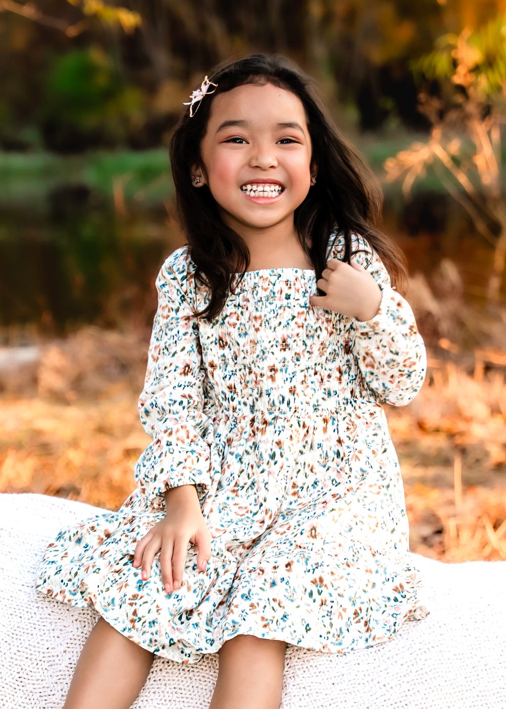 A child in a floral print dress sits outdoors during golden hour creating a joyful and playful atmosphere.