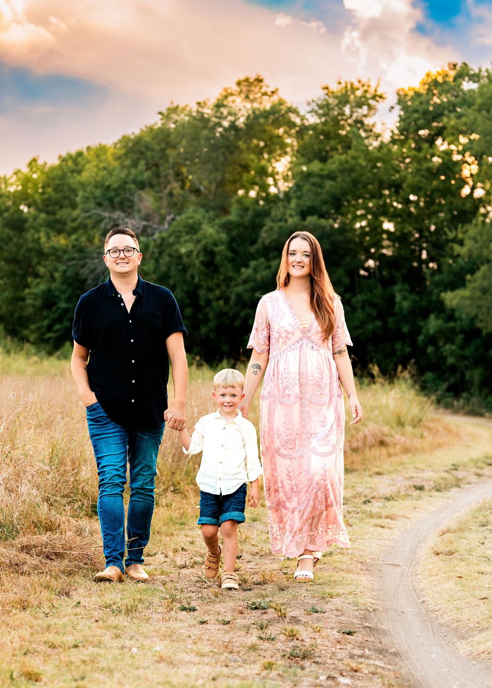 A family walks together on a dirt path through tall grass at sunset creating a warm and intimate outdoor scene.