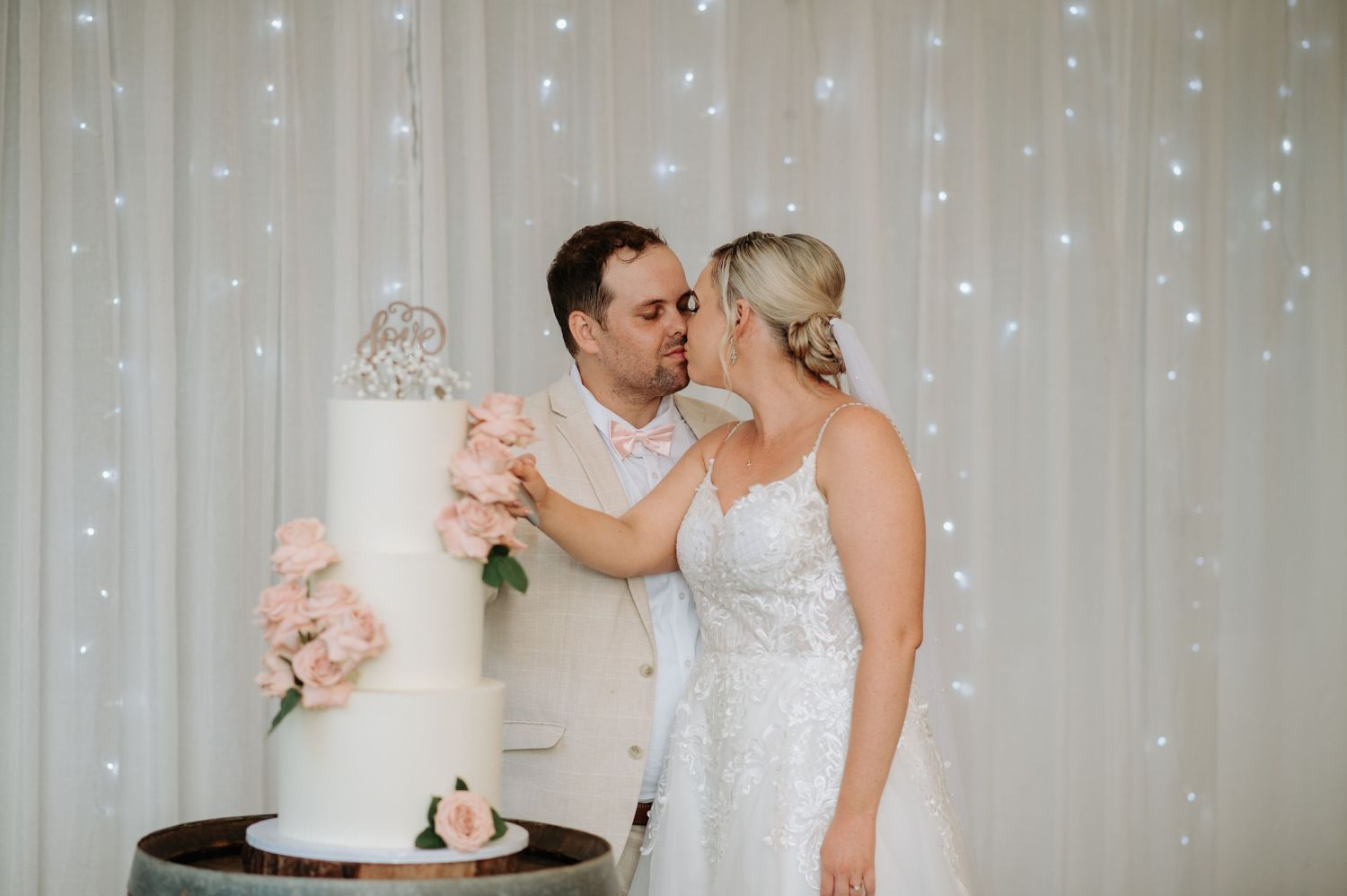 Couple cuts elegant white wedding cake against sparkly backdrop.