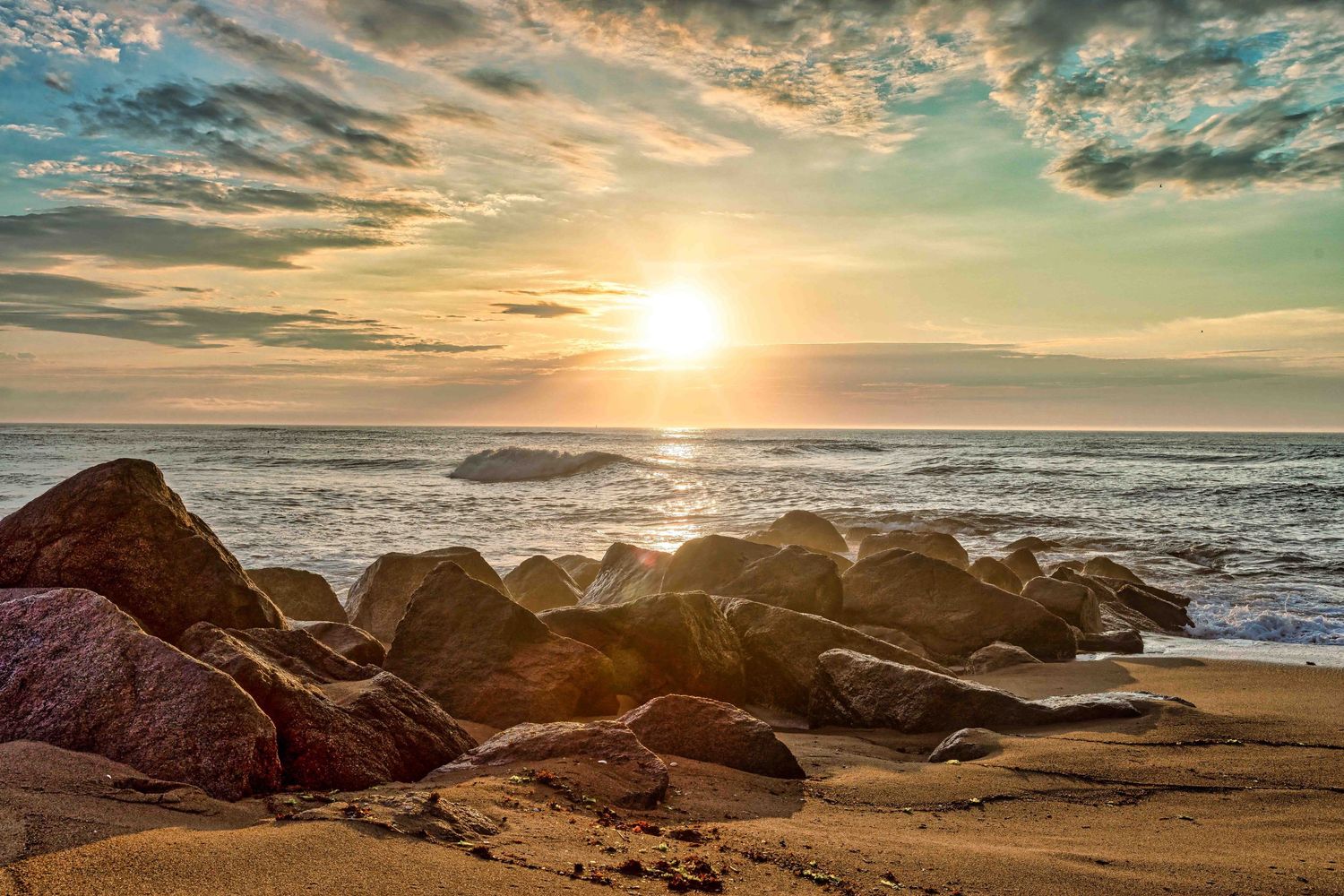 Dramatic sunset over rocky coastline with waves crashing against shore.