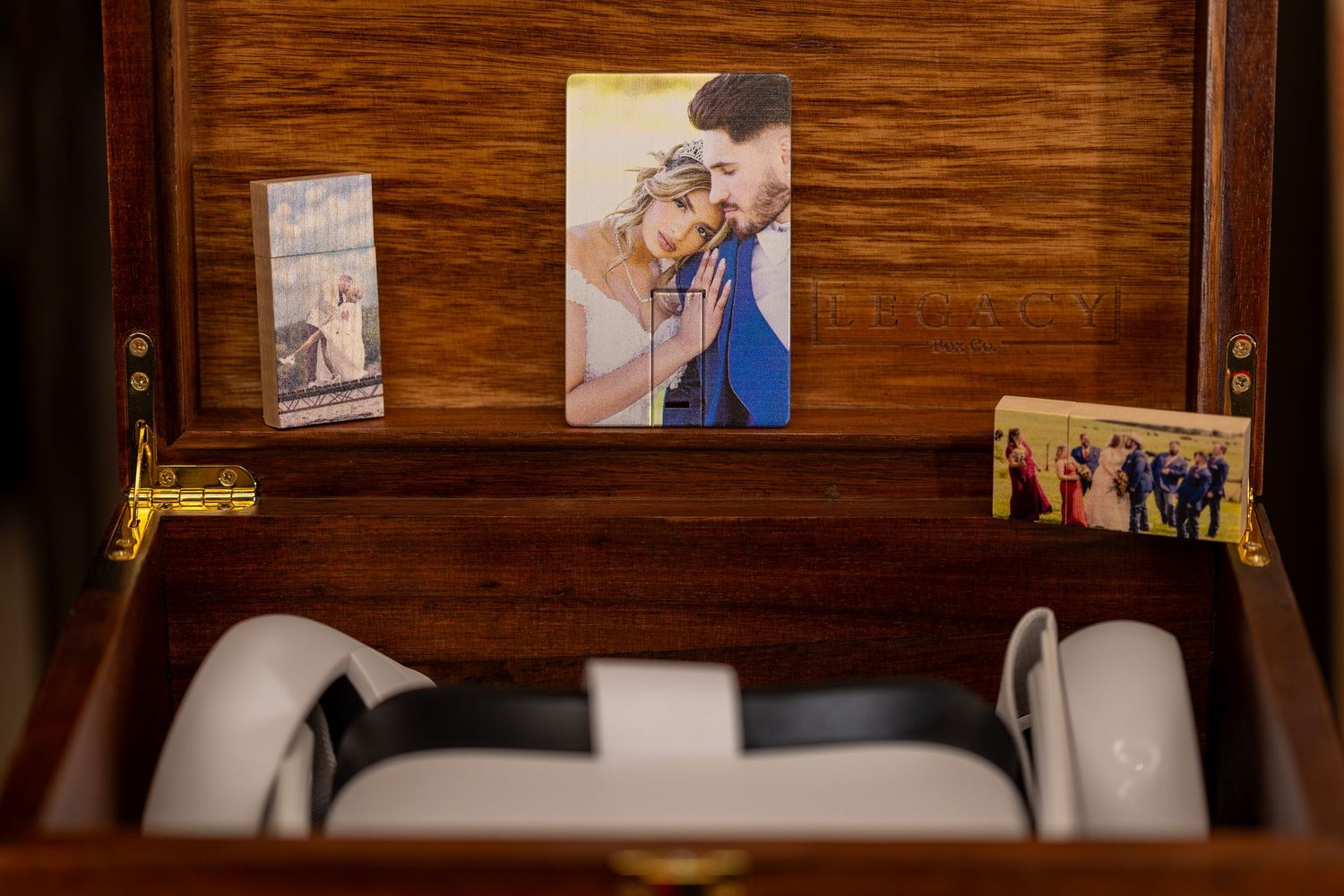 A wooden box interior containing photographs and white electronic devices.