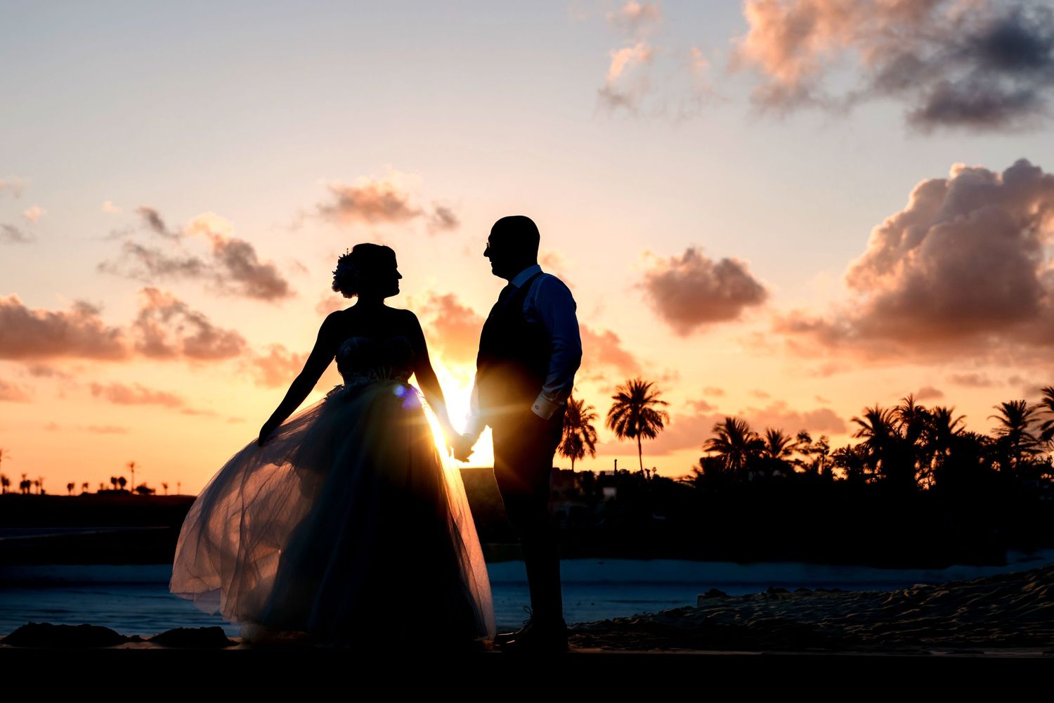 Silhouettes of couple against vibrant sunset sky with palm trees.