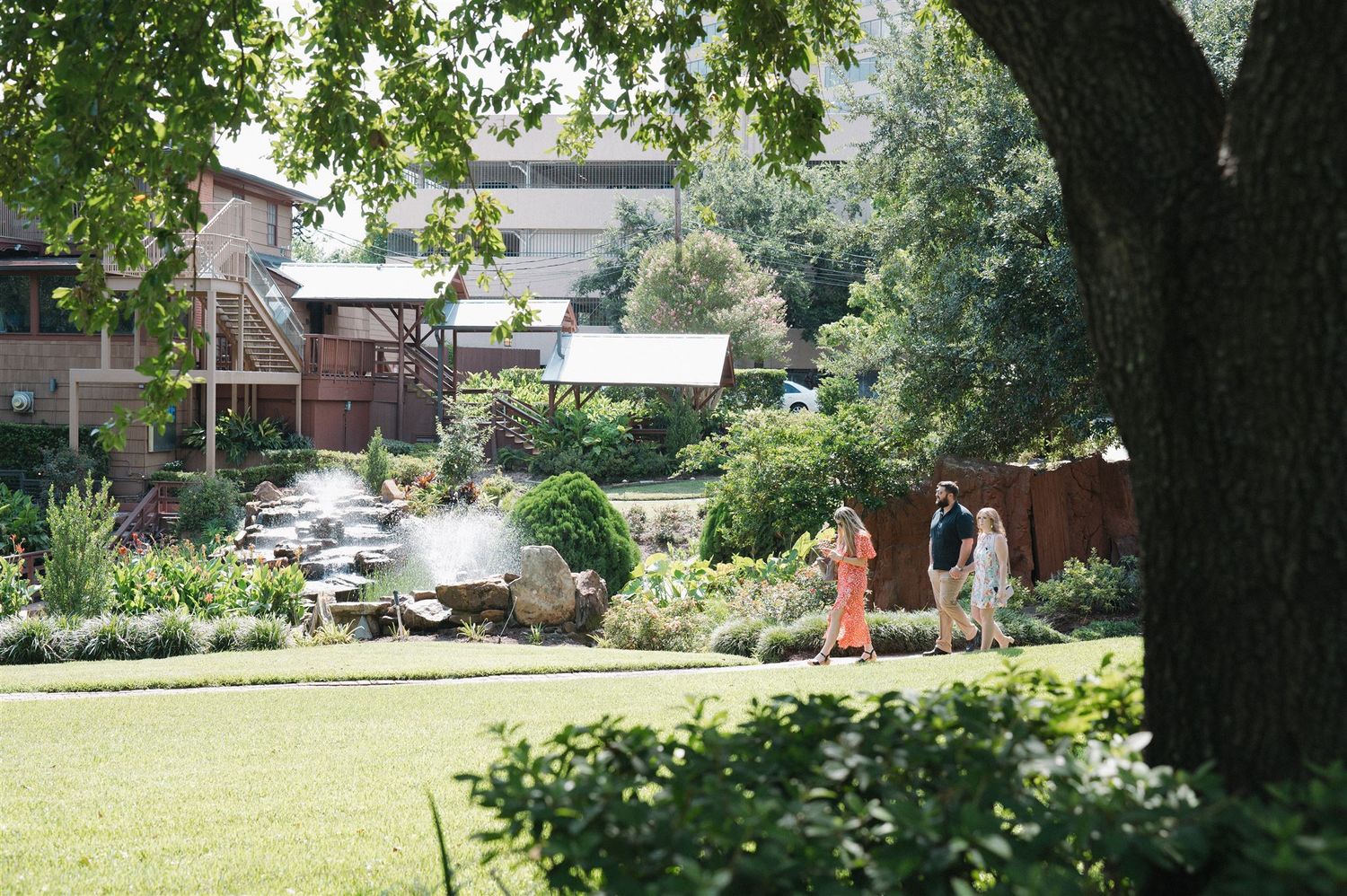 A peaceful garden landscape with a lawn and mature trees surrounding a terrace area on a sunny day.