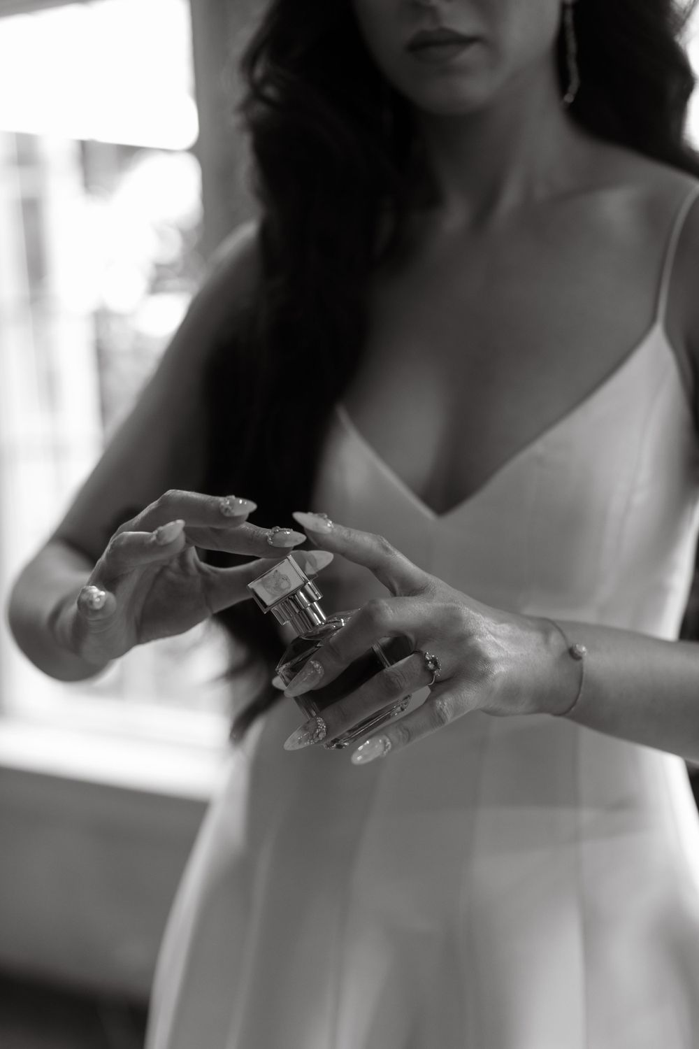 Bride in white dress holding perfume bottle in black and white photography.