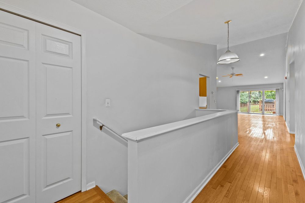 Bright hallway with hardwood floors, white walls, vaulted ceiling, and view into open living area.
