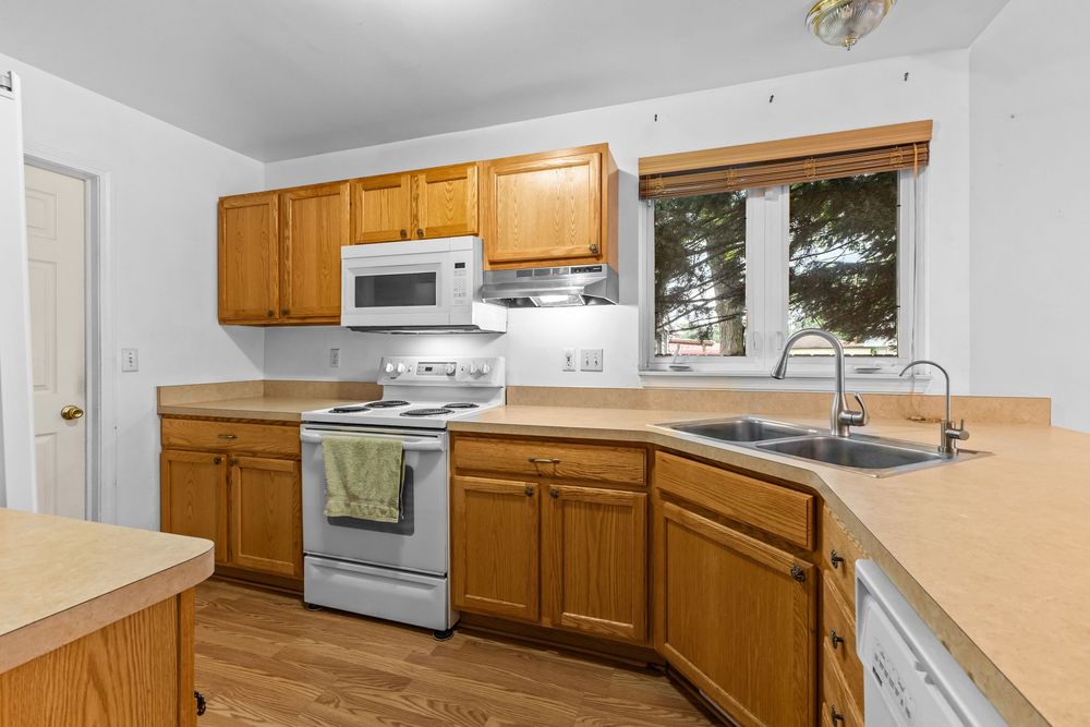 Kitchen with oak cabinets, white appliances, corner sink, and hardwood floors with natural window light.