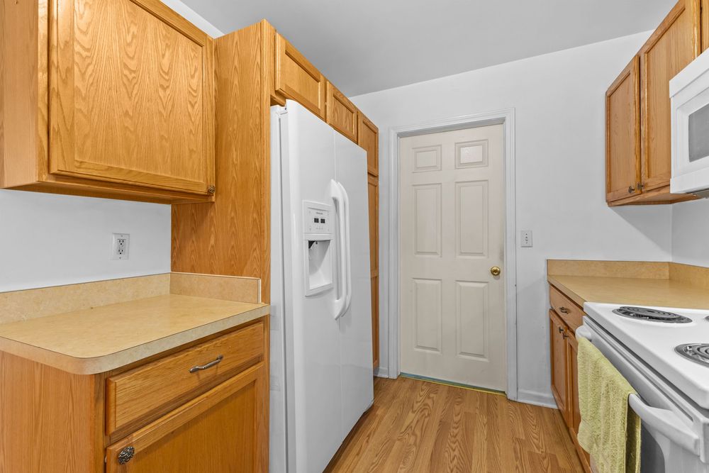 Kitchen with oak cabinetry, white refrigerator with ice maker, and light wood laminate flooring.
