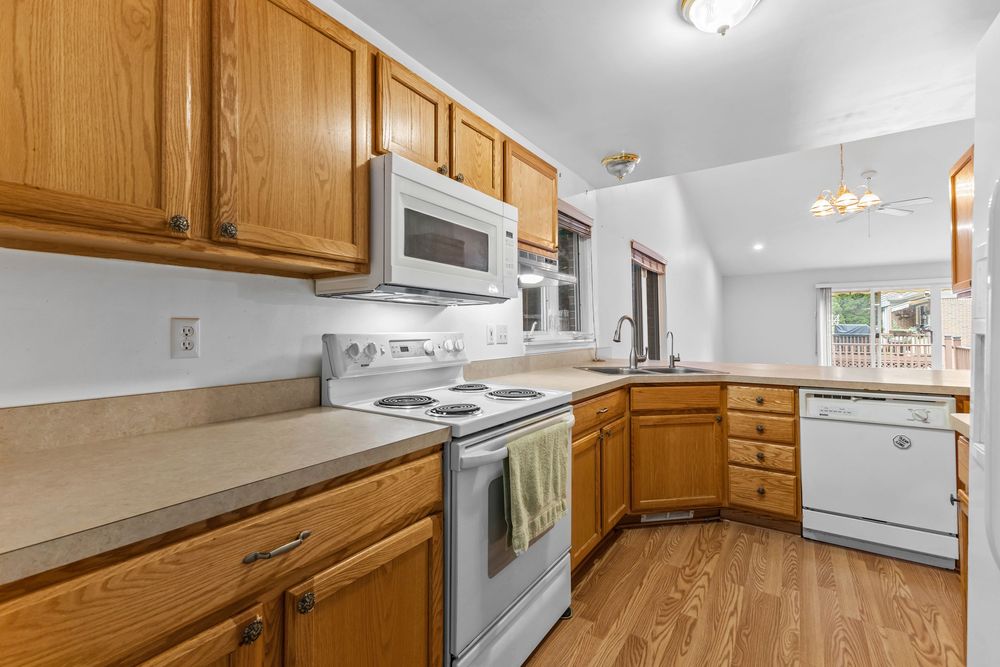 Kitchen featuring oak cabinets, white appliances including stove and dishwasher, and hardwood floors.