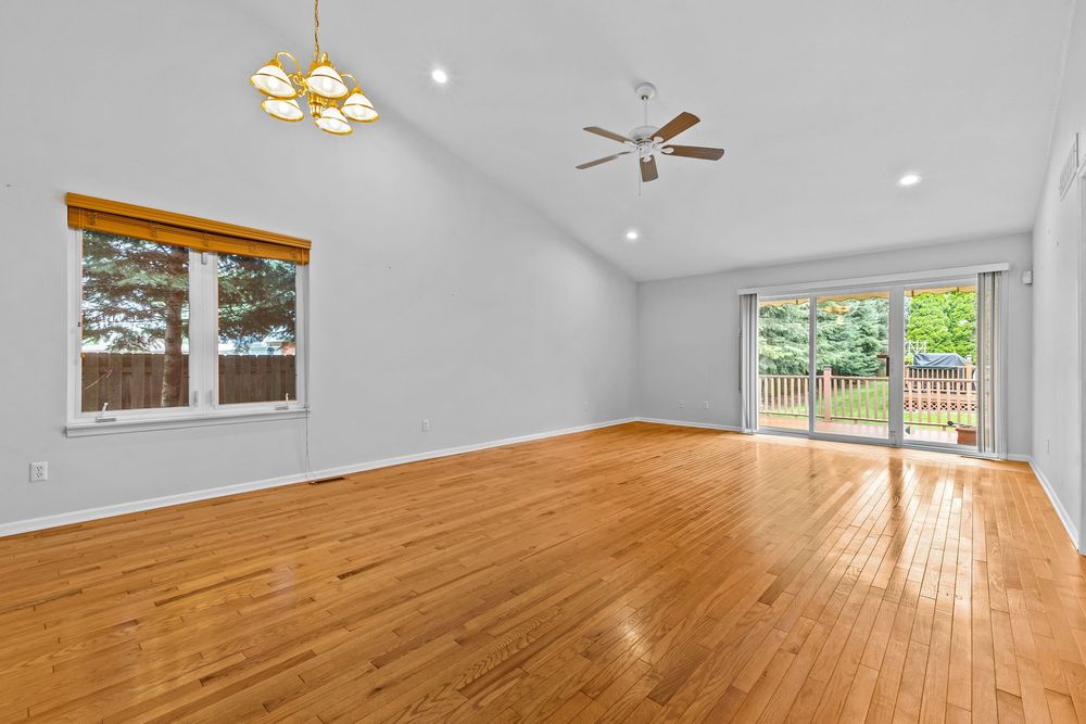 Spacious living room with vaulted ceiling, hardwood floors, two ceiling fans, and sliding glass doors.