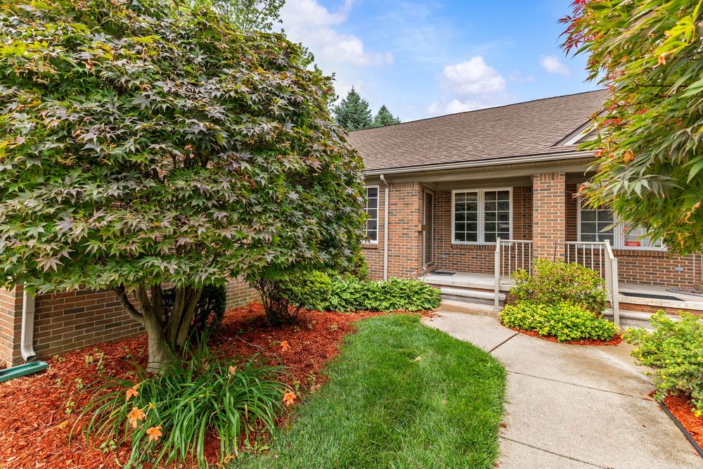 Brick ranch home entrance with mature Japanese maple trees and manicured landscaping.