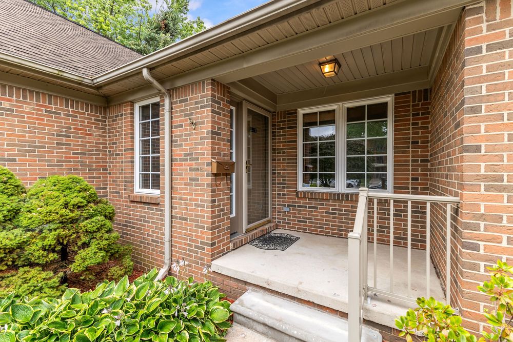Close-up of brick home entry with covered porch, large windows, and lush greenery.