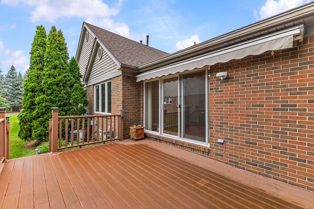 Expansive wood deck with retractable awning attached to a brick home with sliding glass patio doors.