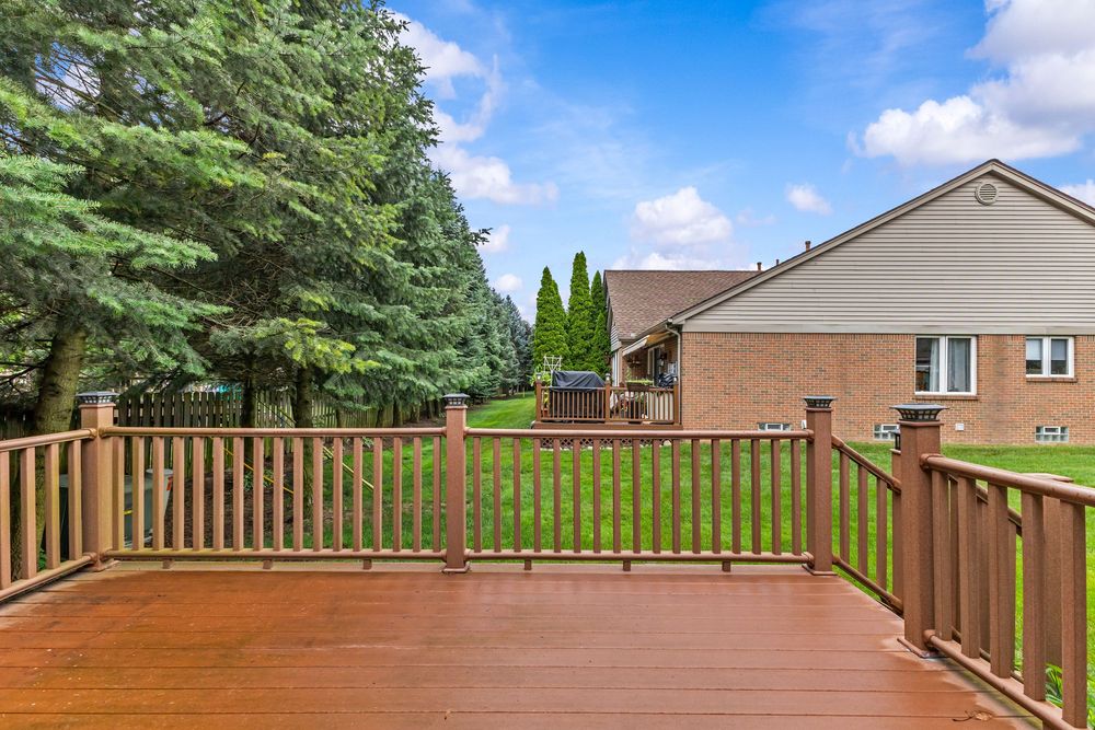 Large wooden deck with brown railings offering views of a green backyard and neighboring brick home.