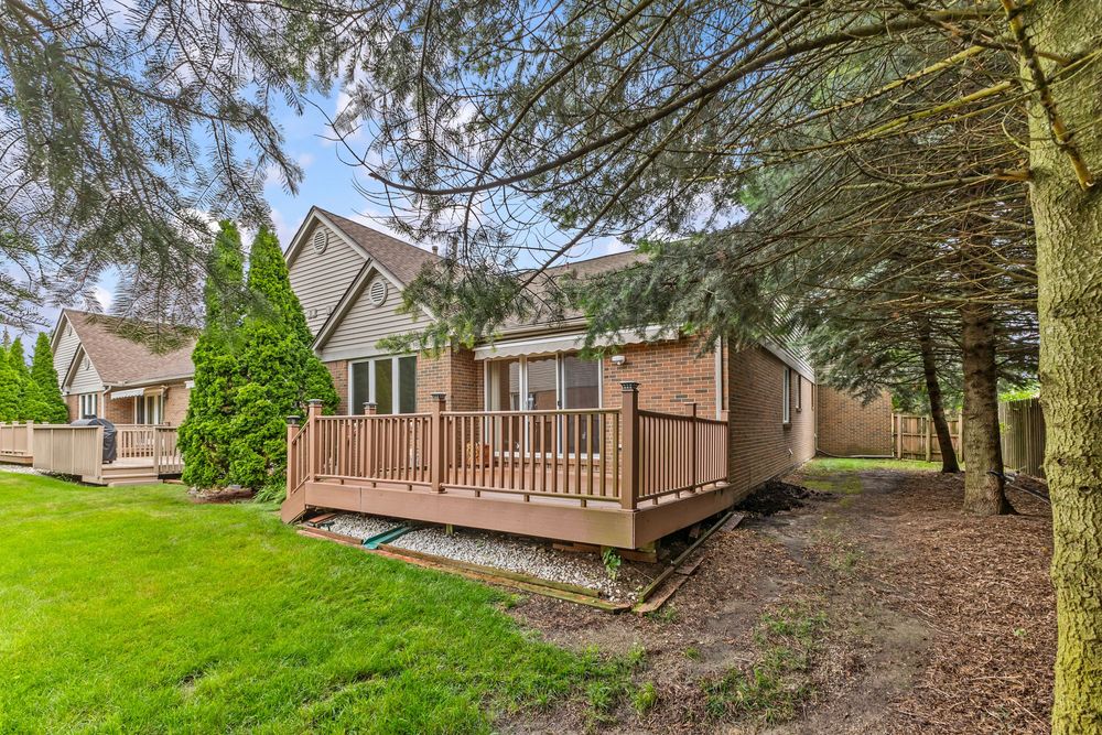 Exterior view of brick home with small wooden deck surrounded by mature evergreen trees and green lawn.