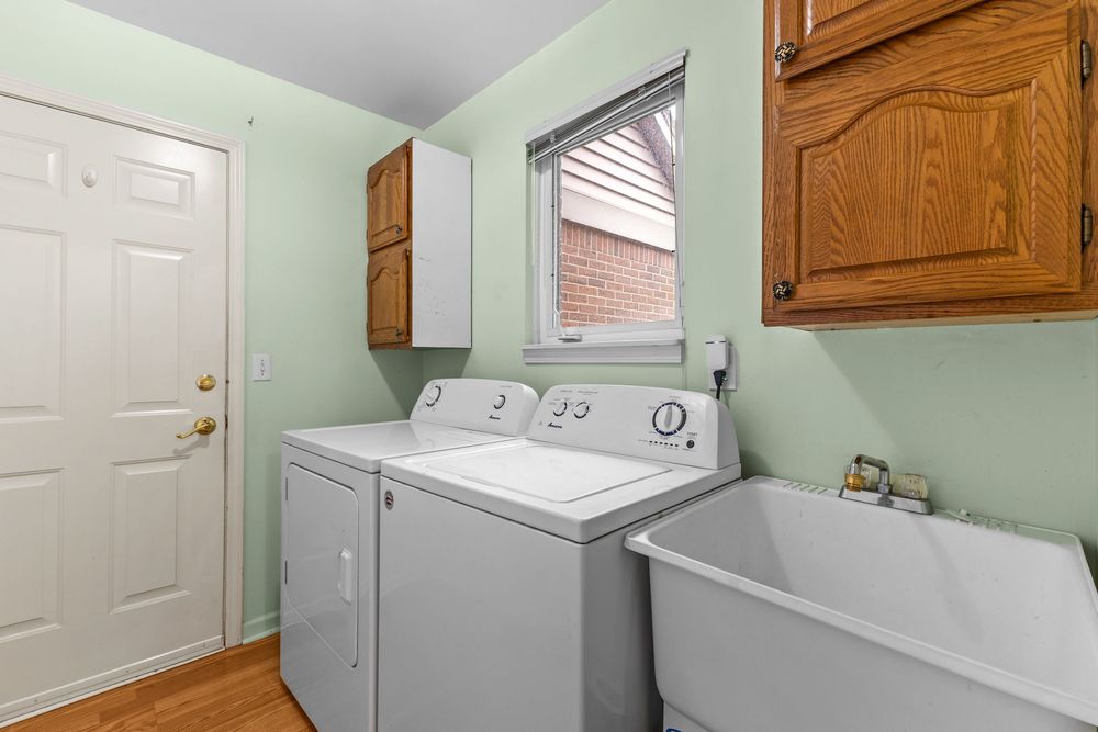 Laundry room with washer and dryer, wood cabinets, utility sink, and window with brick exterior view.