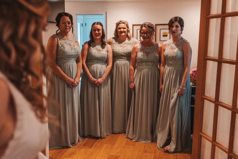 Bridesmaids pose in elegant dove gray dresses with lace details at a wedding venue.