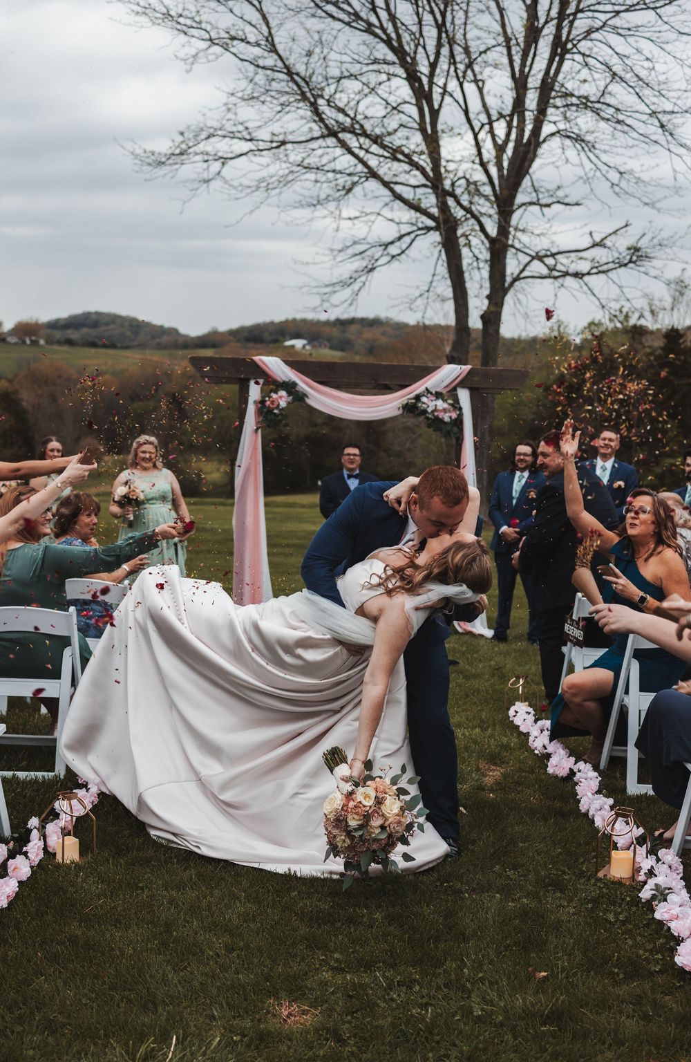 Wedding ceremony guests reacting joyfully as newlyweds share their first kiss outdoors.