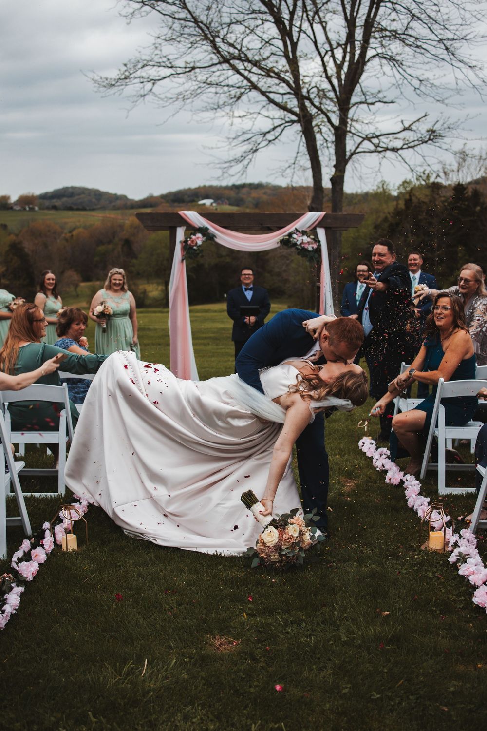 Wedding party throwing flower petals while walking down the aisle at an outdoor fall ceremony.