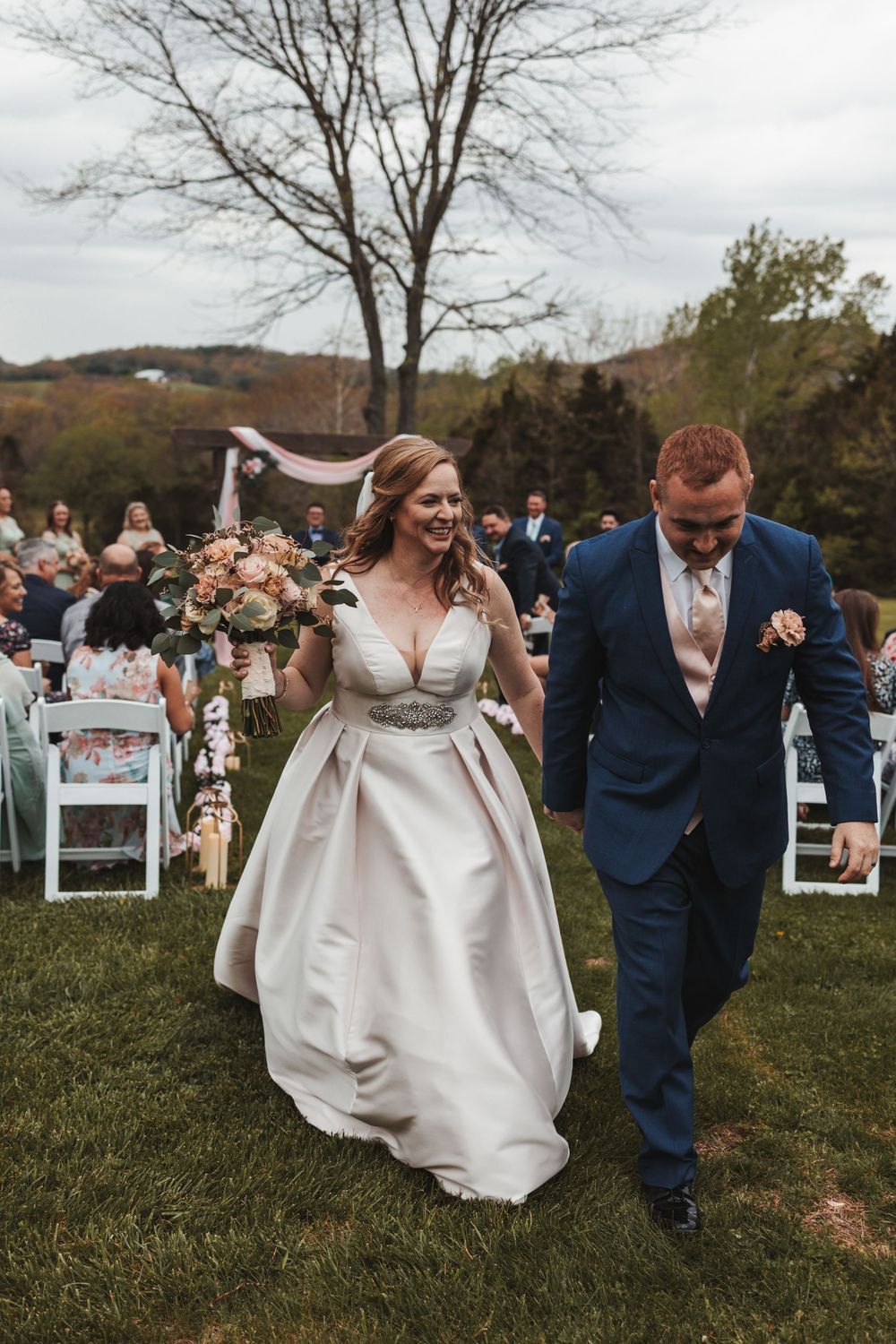 Wedding party celebrating and dancing down an outdoor aisle decorated with white chairs and pink accents.